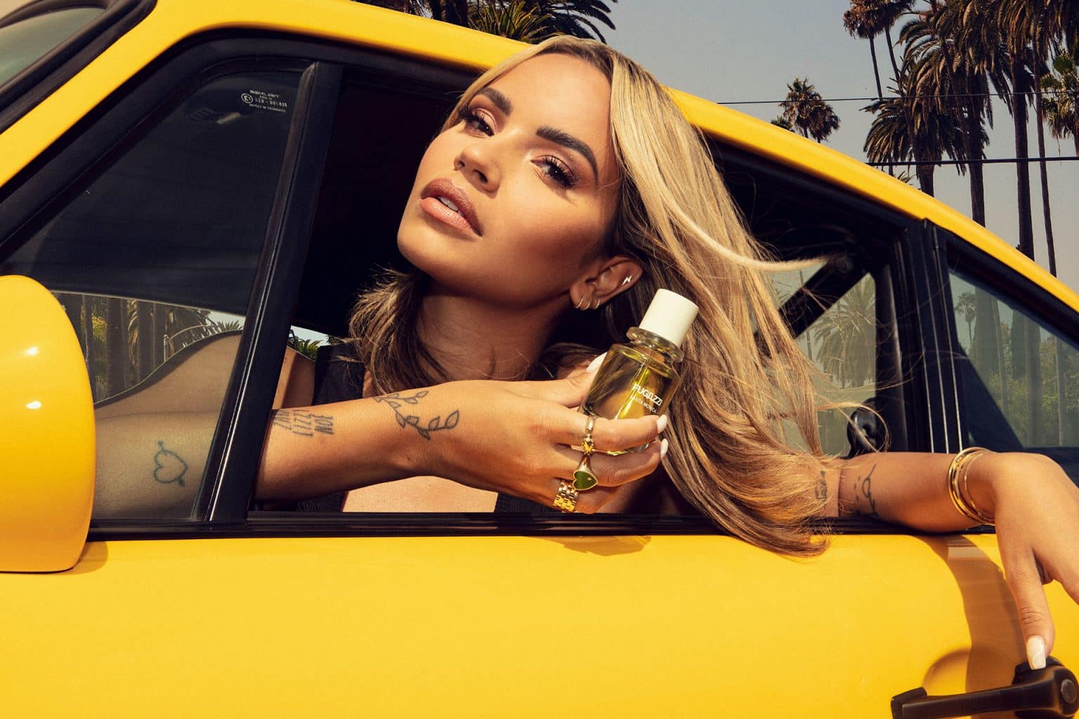 Monica holding a bottle of Fugazzi fragrance in a yellow car